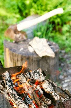 firewood burning in outdoor brazier close up with ax in stump on background