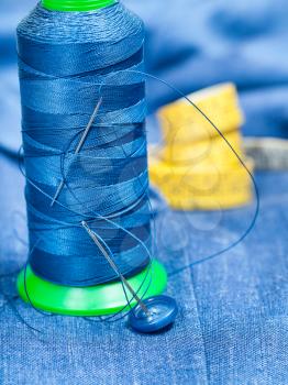 tailoring still life - thread bobbin with needles, button, measure tape on blue silk textile