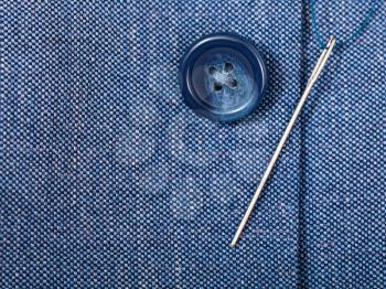 attaching of button to blue silk tissue by needle close up