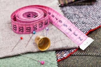 dressmaking still life - pink measure tape, pins, thimble on textile