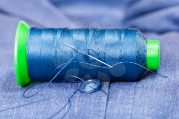tailoring still life - thread bobbin with needle, button on blue silk jacket