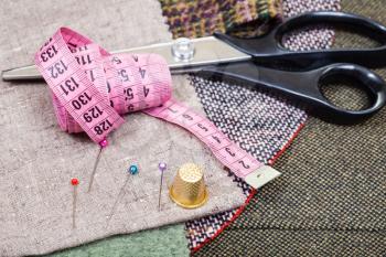 dressmaking still life - pink measure tape, pins, thimble, shears on fabrics