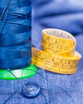 tailoring still life - thread bobbin with needle, button, measure tape on blue silk dress