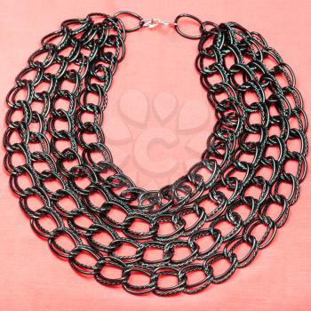 top view of necklace from strings of black chain on pink textile background