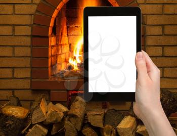 comfortable holiday concept - tourist photographs fireplace on tablet pc with cut out screen with blank place for advertising