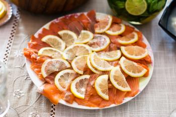 plate with sliced salted smoked salmon fish with lemons on served table
