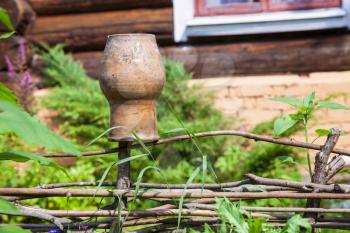 rural scenery - wattle fence with old clay pot and country log house