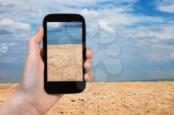 travel concept - tourist photographs of shelly and sand beach of Azov Sea on smartphone