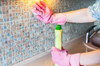 House cleaning - woman washes ceramic tiles on kitchen wall with detergent