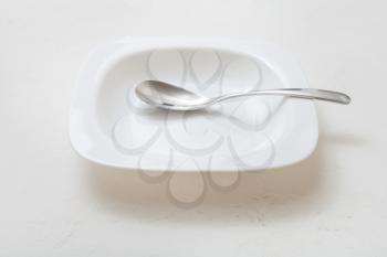 square white bowl with spoon on plastering surface