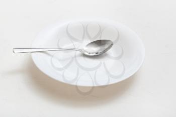 white deep plate with steel spoon on plastering surface