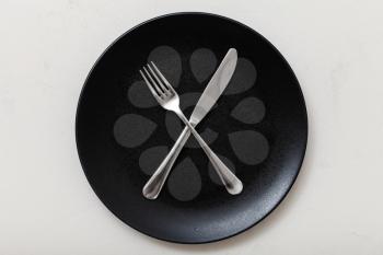 food concept - top view of black plate with crossing knife, spoon on white plastering board