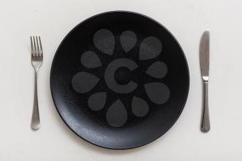 food concept - top view of black plate with knife, spoon on white plastering board