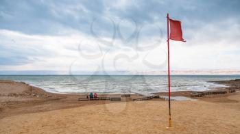 Travel to Middle East country Kingdom of Jordan - red flag on beach of Dead Sea in windy day in winter season