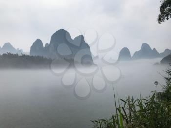 travel to China - green grass on riverbed and background from fog on river near Xingping town in Yangshuo county in spring morning