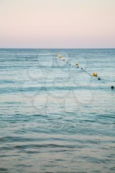 Travel to Algarve Portugal - buoys in water of Atlantic ocean on beach Praia Maria Luisa near Albufeira city in pink evening twilight