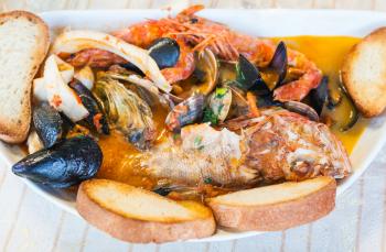 typical italian food - top view of bowl with fish soup with seafood in sicilian restaurant