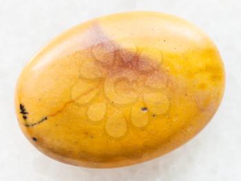 macro shooting of natural mineral rock specimen - bead from yellow Mookaite (Mookaite Jasper) gemstone from Australia on white marble background