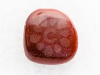 macro shooting of mineral rock specimen - tumbled red goldstone gemstone on white marble background