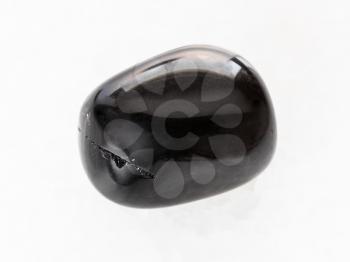macro shooting of natural mineral rock specimen - tumbled black Onyx gemstone on white marble background