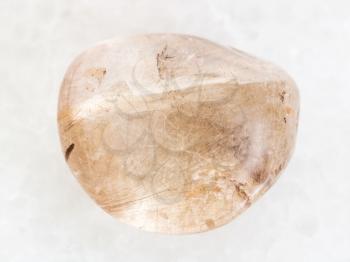 macro shooting of natural mineral rock specimen - polished Rutilated Quartz gemstone on white marble background