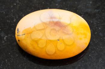 macro shooting of natural mineral rock specimen - bead from yellow Mookaite (Mookaite Jasper) gemstone on dark granite background