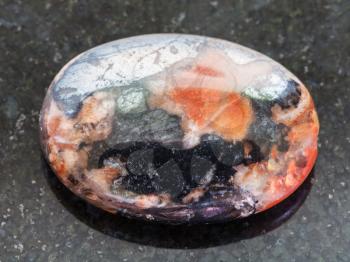 macro shooting of natural mineral rock specimen - cabochon from Hematite and mookaite gemstones on dark granite background