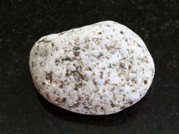 macro shooting of natural mineral rock specimen - tumbled of white Granite stone on dark granite background