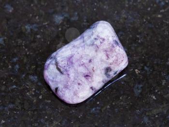 macro shooting of natural mineral rock specimen - tumbled Amethyst gemstone on dark granite background from Brazil