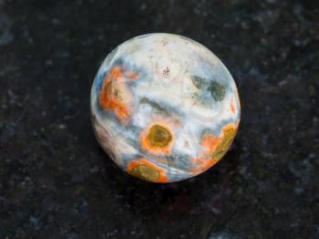 macro shooting of natural mineral rock specimen - tumbled orbicular jasper gemstone on dark granite background