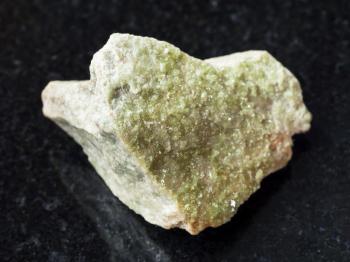 macro shooting of natural mineral rock specimen - green Vesuvianite crystals on rough stone on dark granite background from Yakutia, Siberia, Russia