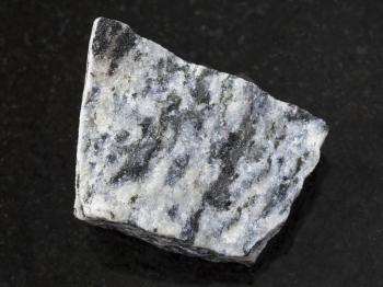 macro shooting of natural mineral rock specimen - raw migmatite stone on dark granite background