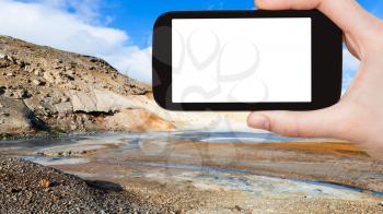 travel concept - tourist photographs mud pot crater in geothermal Krysuvik area on Southern Peninsula (Reykjanesskagi, Reykjanes) in Iceland on smartphone with cut out screen for advertising logo
