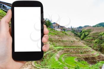 travel concept - tourist photographs Rice Terraces in Dazhai village in Longsheng (Dragon's Backbone, Longji) county in China in spring season on smartphone with cut out screen for advertising logo