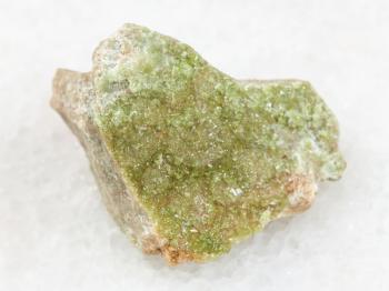 macro shooting of natural mineral rock specimen - green Vesuvianite crystals on rough stone on white marble background from Yakutia, Siberia, Russia