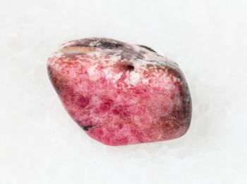 macro shooting of natural mineral rock specimen - tumbled pink rhodonite gem stone on white marble background from Ural mountains in Russia