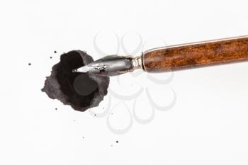 top view of brown nib pen over black ink blot on white paper