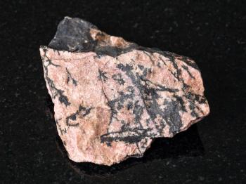 macro shooting of natural mineral - rough Rhodonite stone on black granite from Ural Mountains