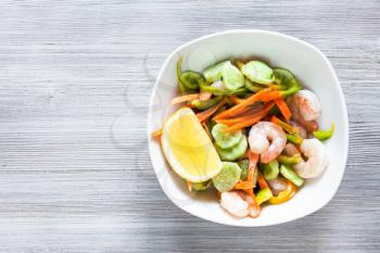 Indian cuisine - prawn salad from fresh vegetables and shrimps in white bowl on gray wooden table with free copyspace