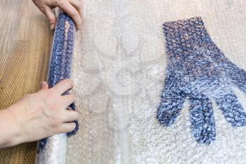 workshop of hand making a fleece gloves from blue Merino sheep wool using wet felting process - craftsman rolls felted gloves in mat for fulling