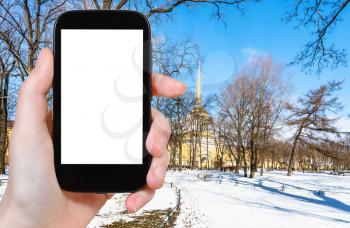 travel concept - tourist photographs of snow-covered path in Alexander Garden in Saint Petersburg city in March on smartphone with empty cutout screen with blank place for advertising