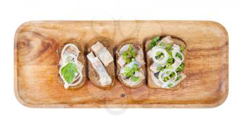 top view of various open sandwich with pickled herring on wooden plate isolated on white background