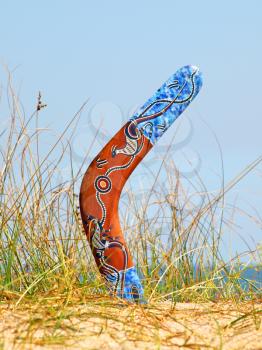 Boomerang on overgrown sandy dune against blue sea and sky.