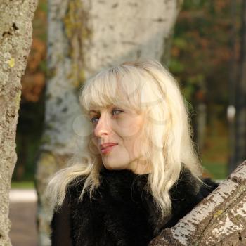 Pretty blonde in black against tree trunk taken closeup.