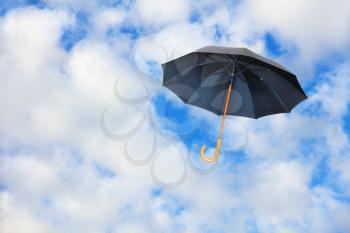 Black umbrella flies in sky against of pure white clouds.Mary Poppins Umbrella.Wind of change concept.