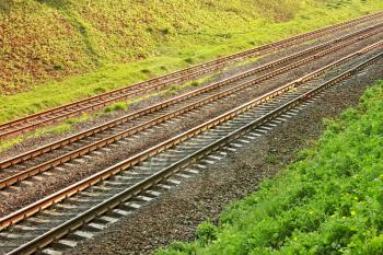 Rail lines in the hollow a bright sunny spring day. Roadside covered with vivid young grass and wild flowers