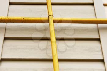 Two mutually perpendicular yellow gas pipes on a background of a wall covered with beige siding