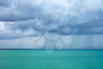 Thick cumulonimbus clouds with rain over the sea with a turquoise surface illuminated by the sun