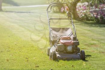 Modern gasoline lawn mower on a green meadow. Gardening equipment