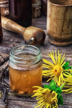 infusion of inflorescences and roots of the medicinal plant Inula on the wooden table next mortar and pestle.Photo tinted.Selective focus